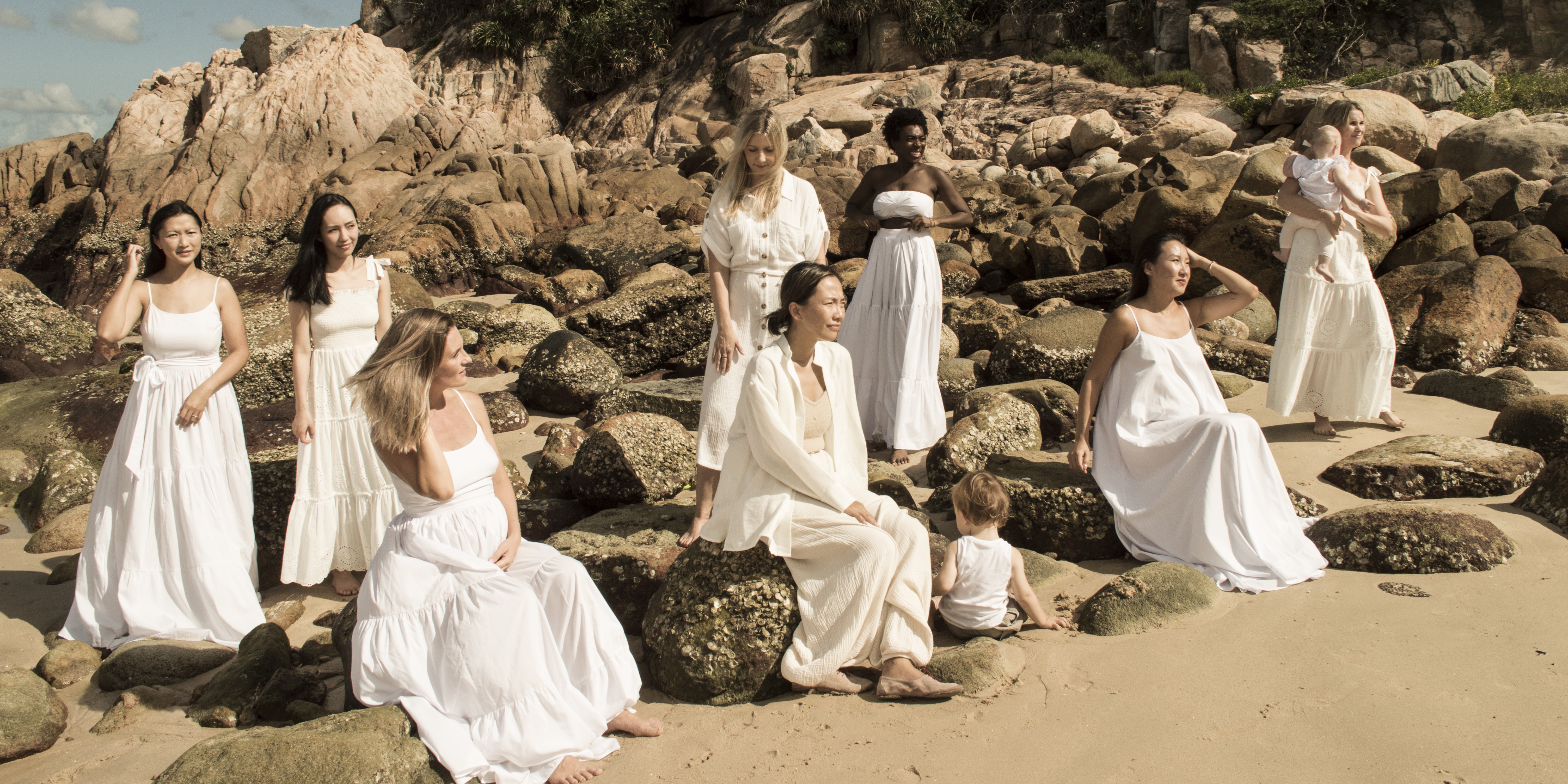 Group of women in white dresses on rocky beach